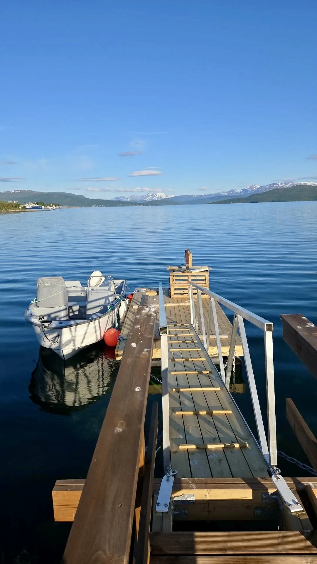 The Senja Fjord Tours boat moored at Finnsnes jetty, ready to depart — snow-capped mountains behind