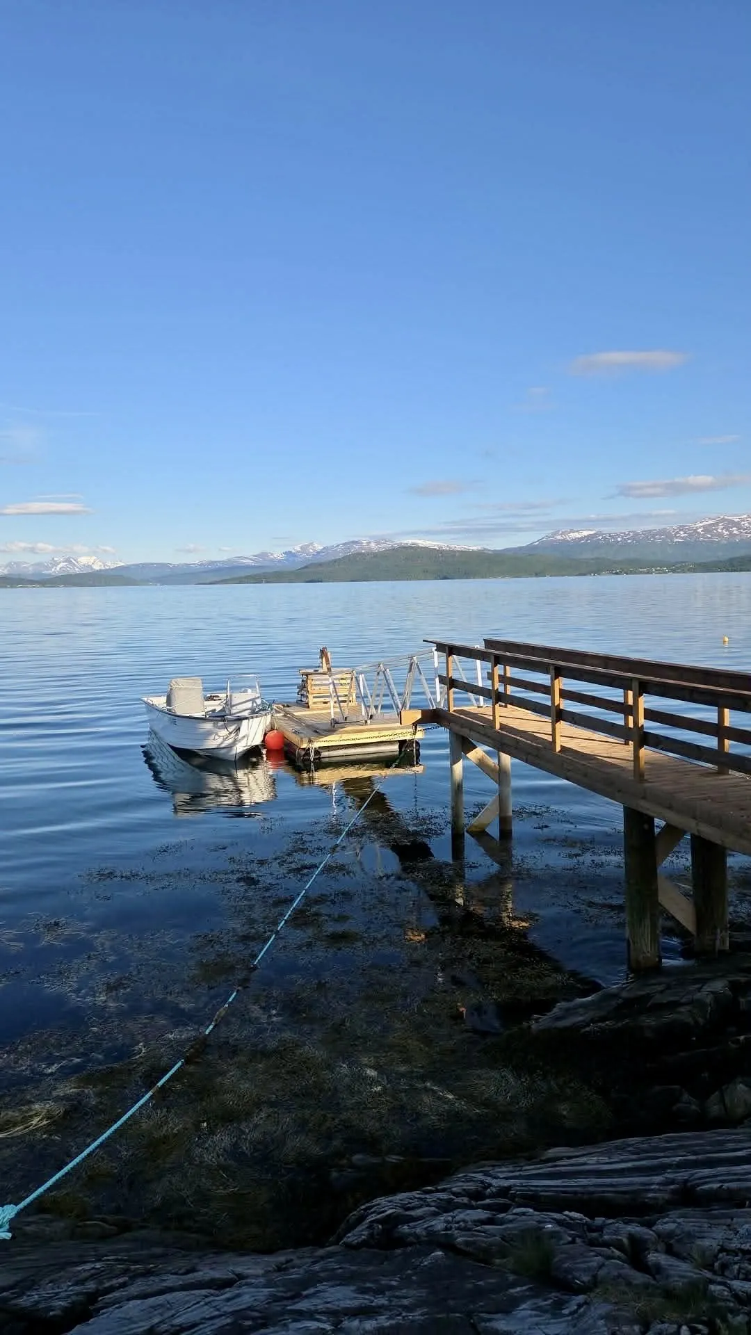 Tour boat tied at the Finnsnes jetty — calm fjord water and snow-capped peaks of Senja beyond