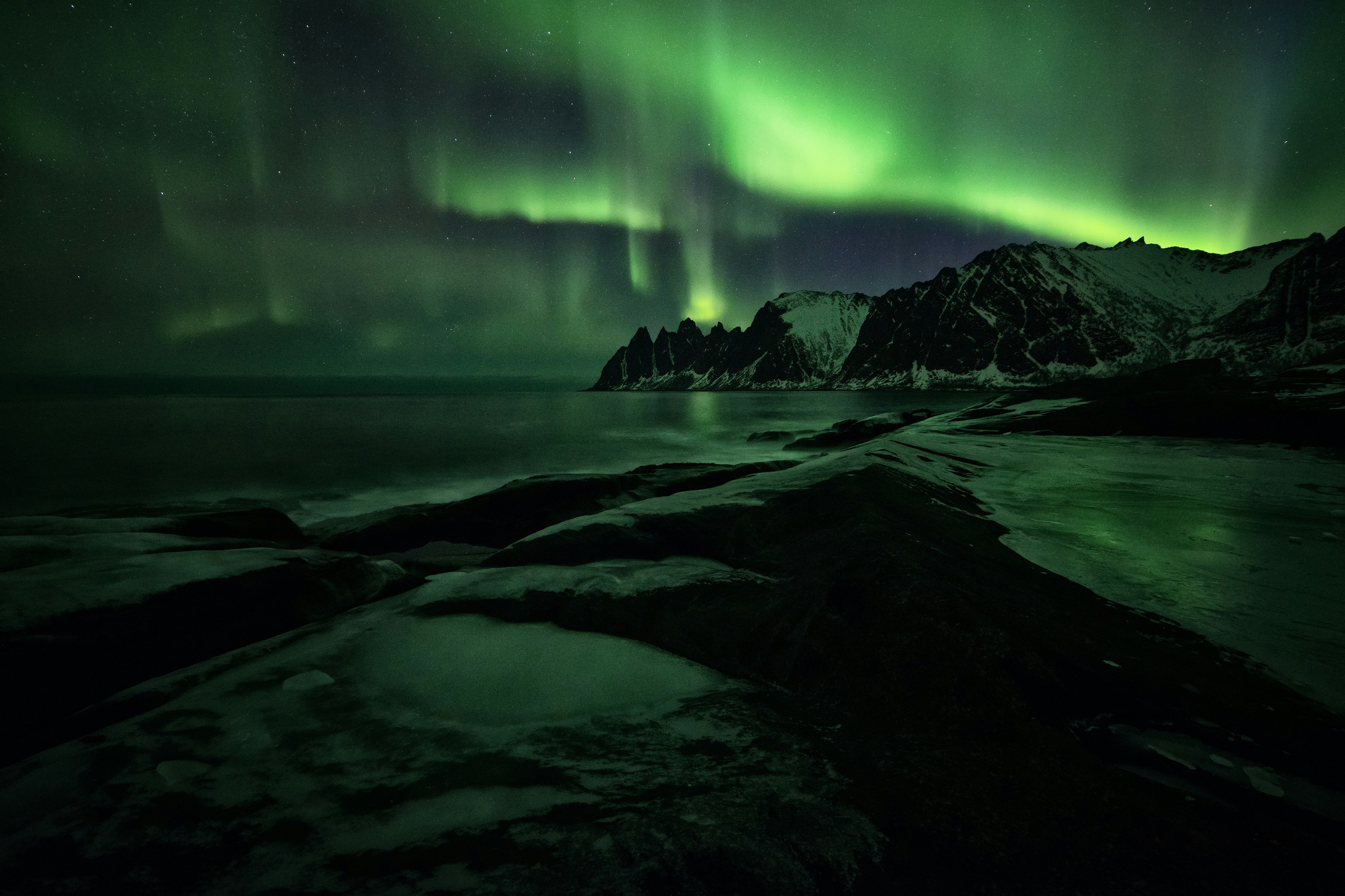 Vivid green aurora borealis over Senja's Okshornan peaks reflected in the dark water below