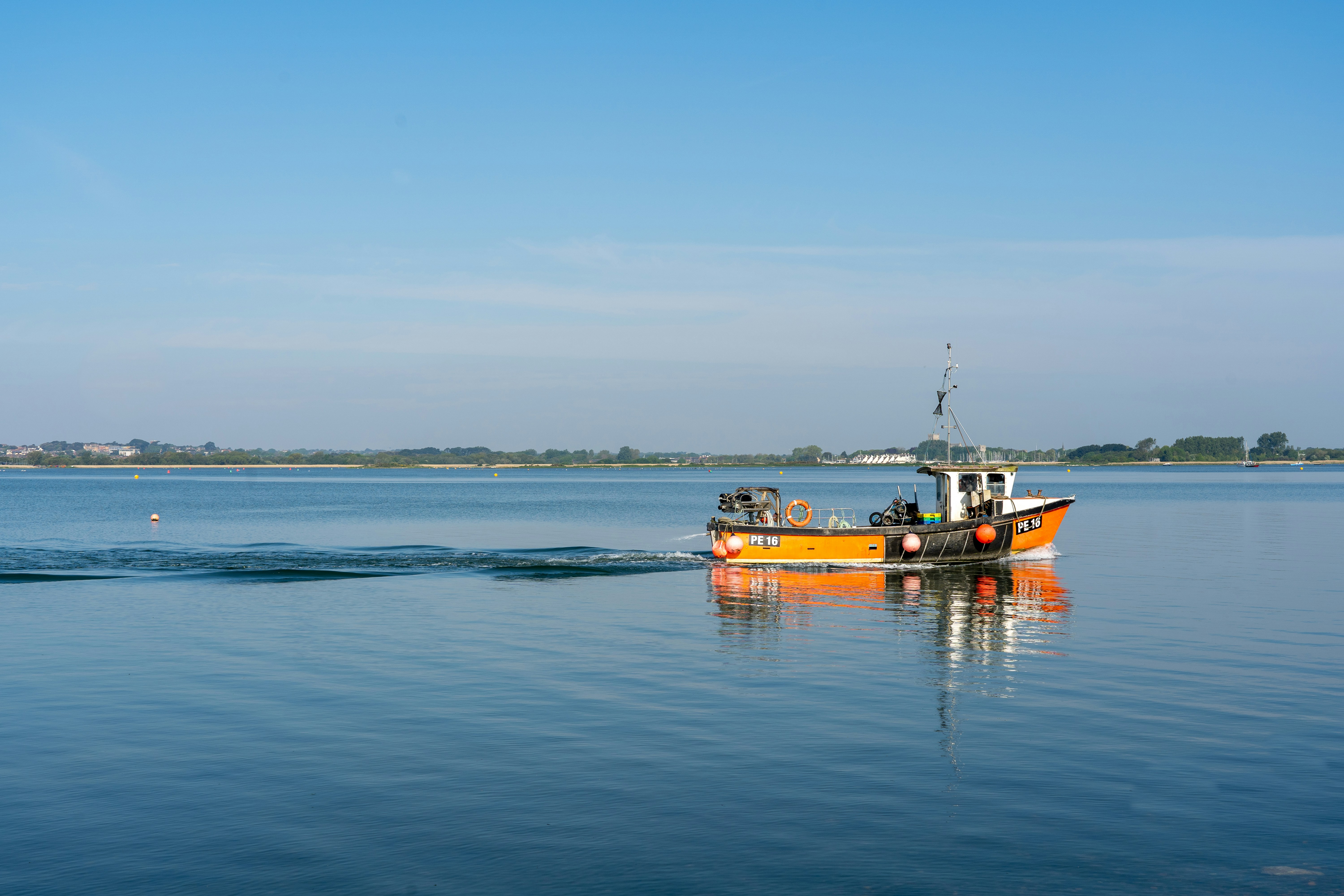 Small orange boat on glassy Arctic water with mountain reflections